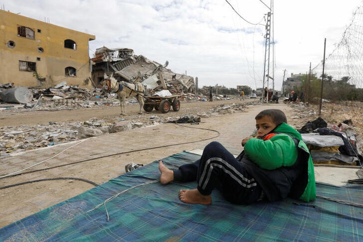 Palestinian boy rests on mattress near ruins of his house which was destroyed by Israeli strikes  in Khan Younis