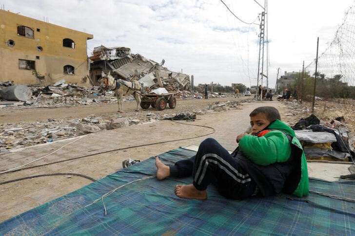 Palestinian boy rests on mattress near ruins of his house which was destroyed by Israeli strikes in Khan Younis