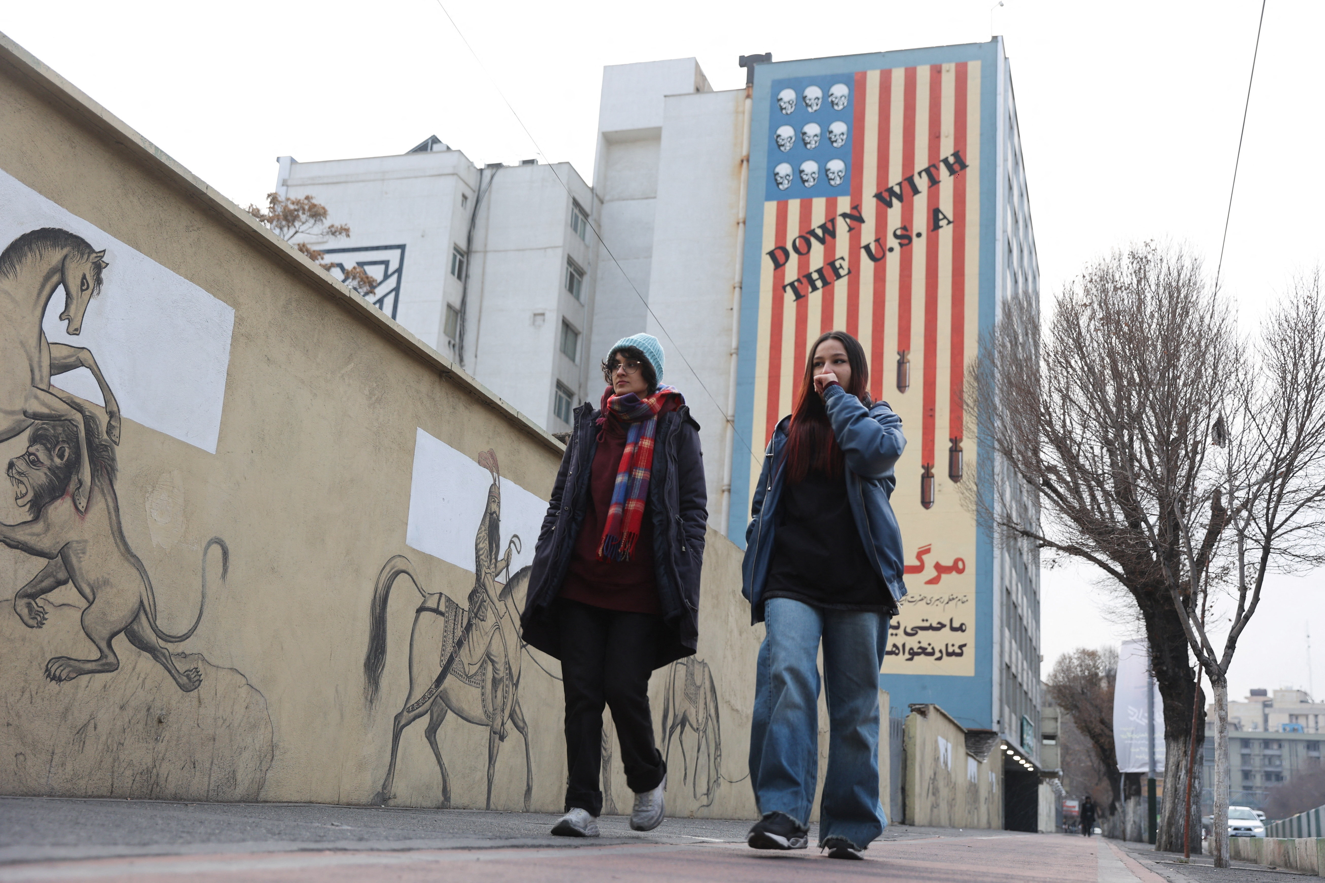 FILE PHOTO: People walk next to an anti-US mural on a street as protests erupt over the collapse of the currency's value in Tehran