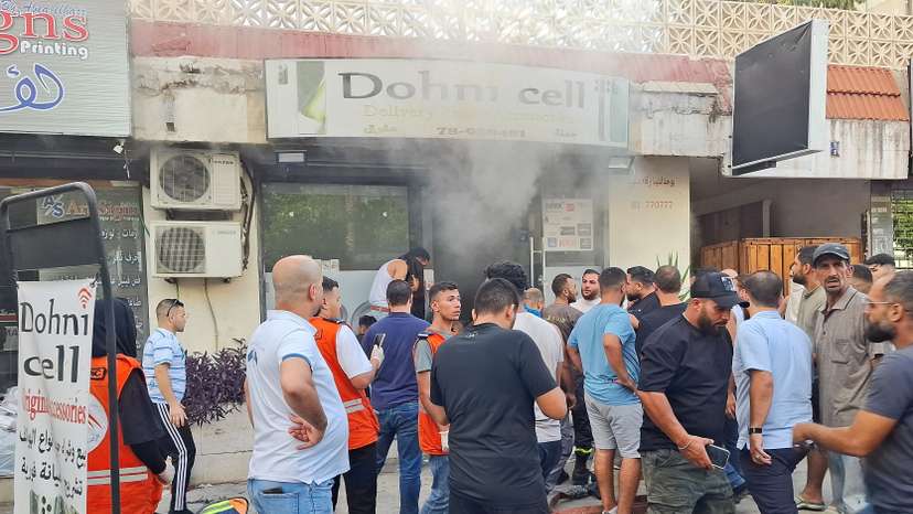 People gather as smoke rises from a mobile shop in Sidon