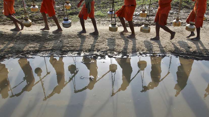 FILE PHOTO: Kanwarias or devotees of Hindu god Shiva carrying pitchers are reflected in a puddle as they walk after filling the pitchers with water from the river Ganges in Allahabad