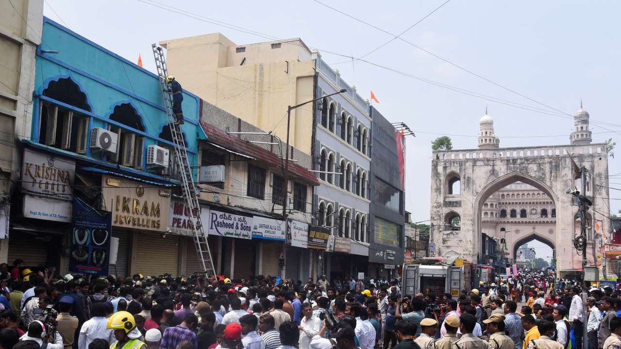 Firefighters, police and crowds stand outside of the building that caught fire in Hyderabad
