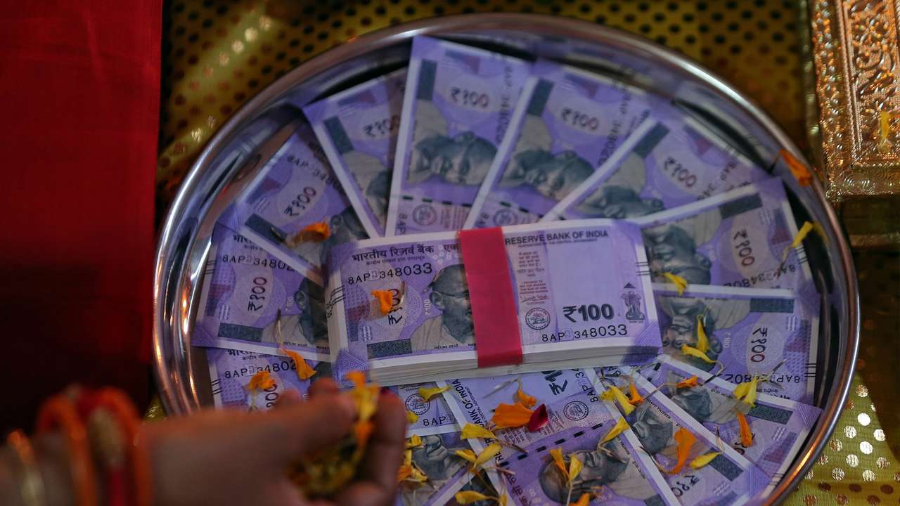 A woman puts flower petals on the new 100 Indian rupee notes as she prays as part of a ritual during Dhanteras, a Hindu festival associated with Lakshmi, the goddess of wealth, in Ahmedabad