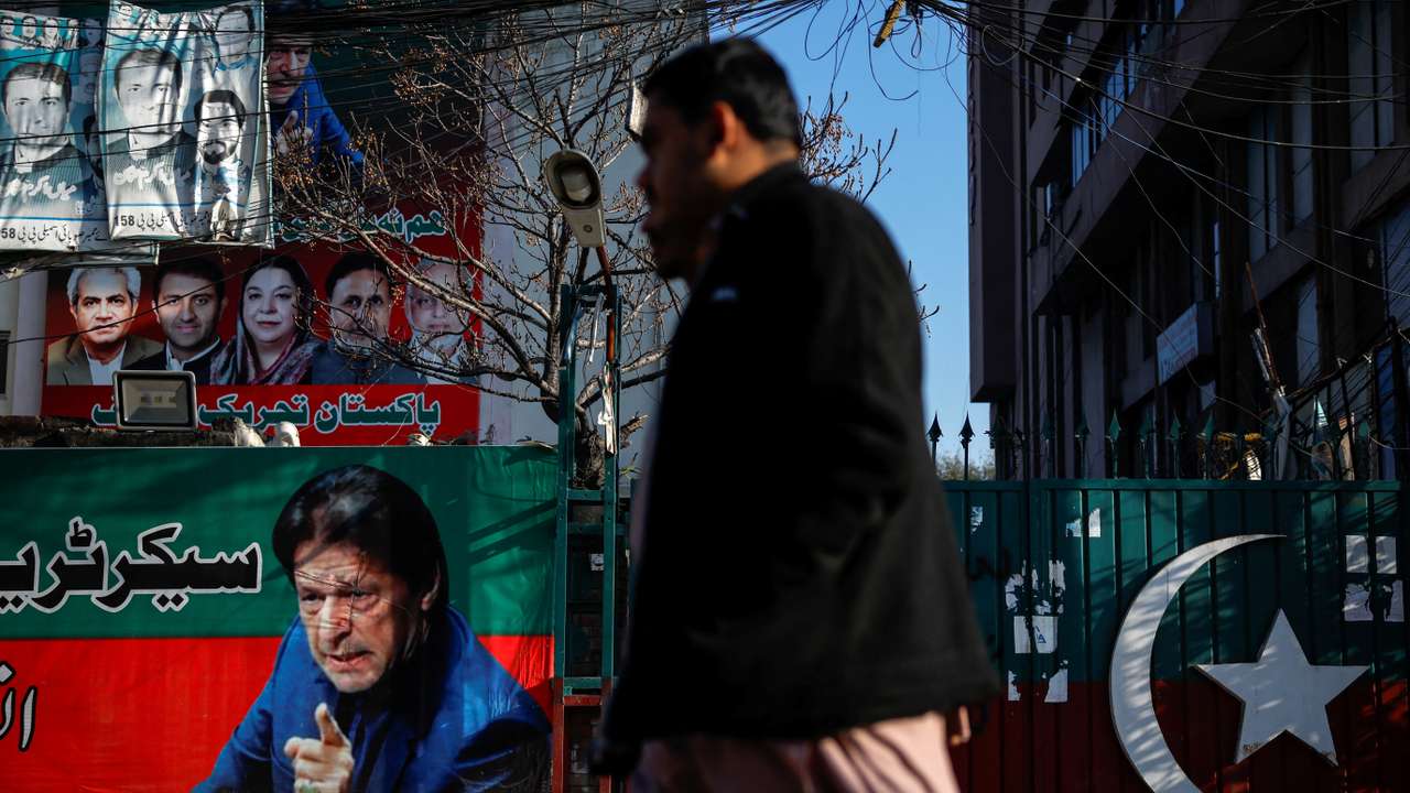 People walk past a banner with a picture of the former Prime Minister Imran Khan outside the party office of Pakistan Tehreek-e-Insaf (PTI), a day after the general election, in Lahore