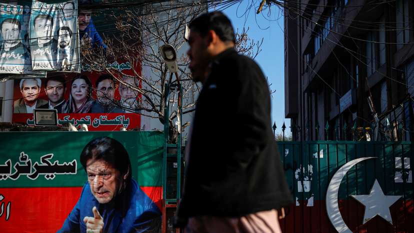 People walk past a banner with a picture of the former Prime Minister Imran Khan outside the party office of Pakistan Tehreek-e-Insaf (PTI), a day after the general election, in Lahore