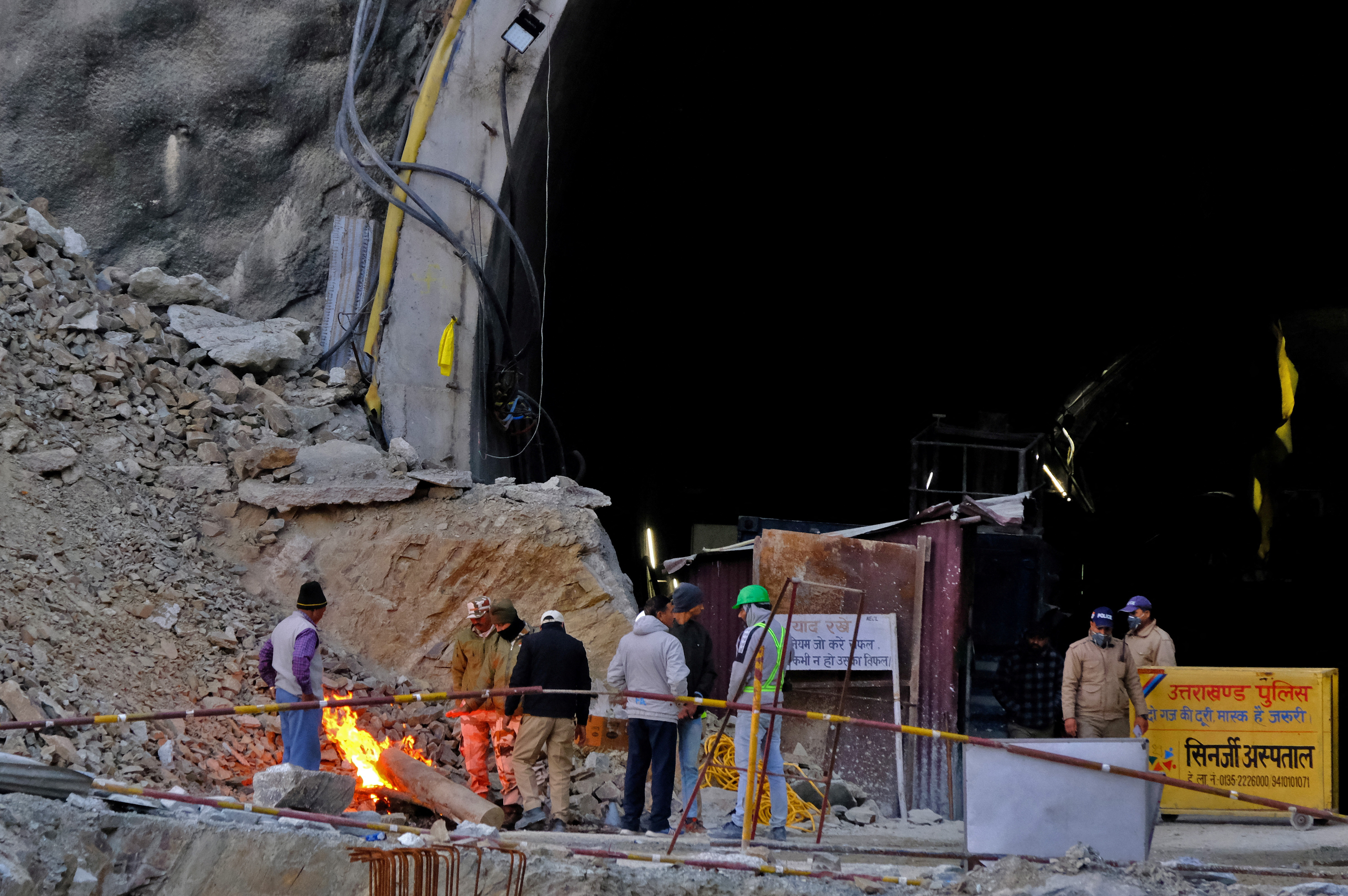 Members of rescue teams and security personnel warm themselves by a bonfire at the entrance of a tunnel where road workers are trapped after a portion of the tunnel collapsed in Uttarkashi