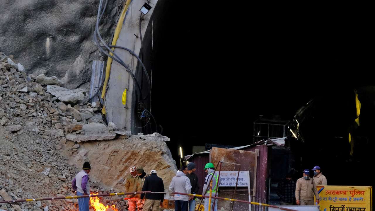 Members of rescue teams and security personnel warm themselves by a bonfire at the entrance of a tunnel where road workers are trapped after a portion of the tunnel collapsed in Uttarkashi