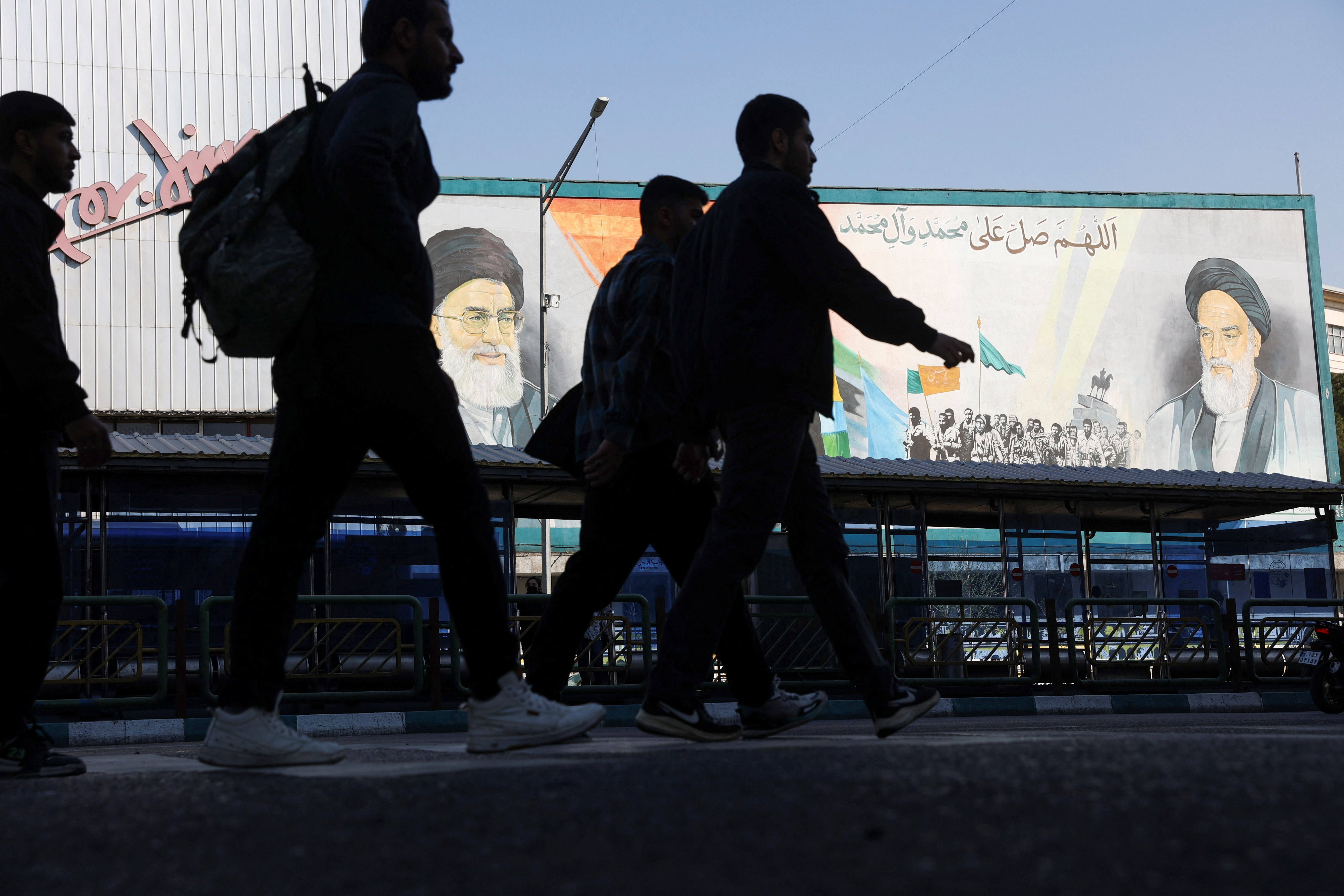 People walk near a mural featuring images of Iran's leaders in Tehran