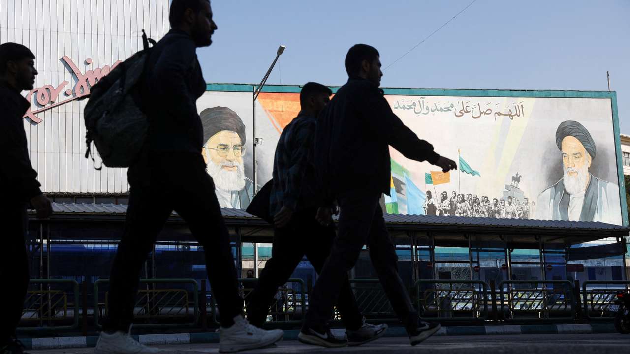People walk near a mural featuring images of Iran's leaders in Tehran