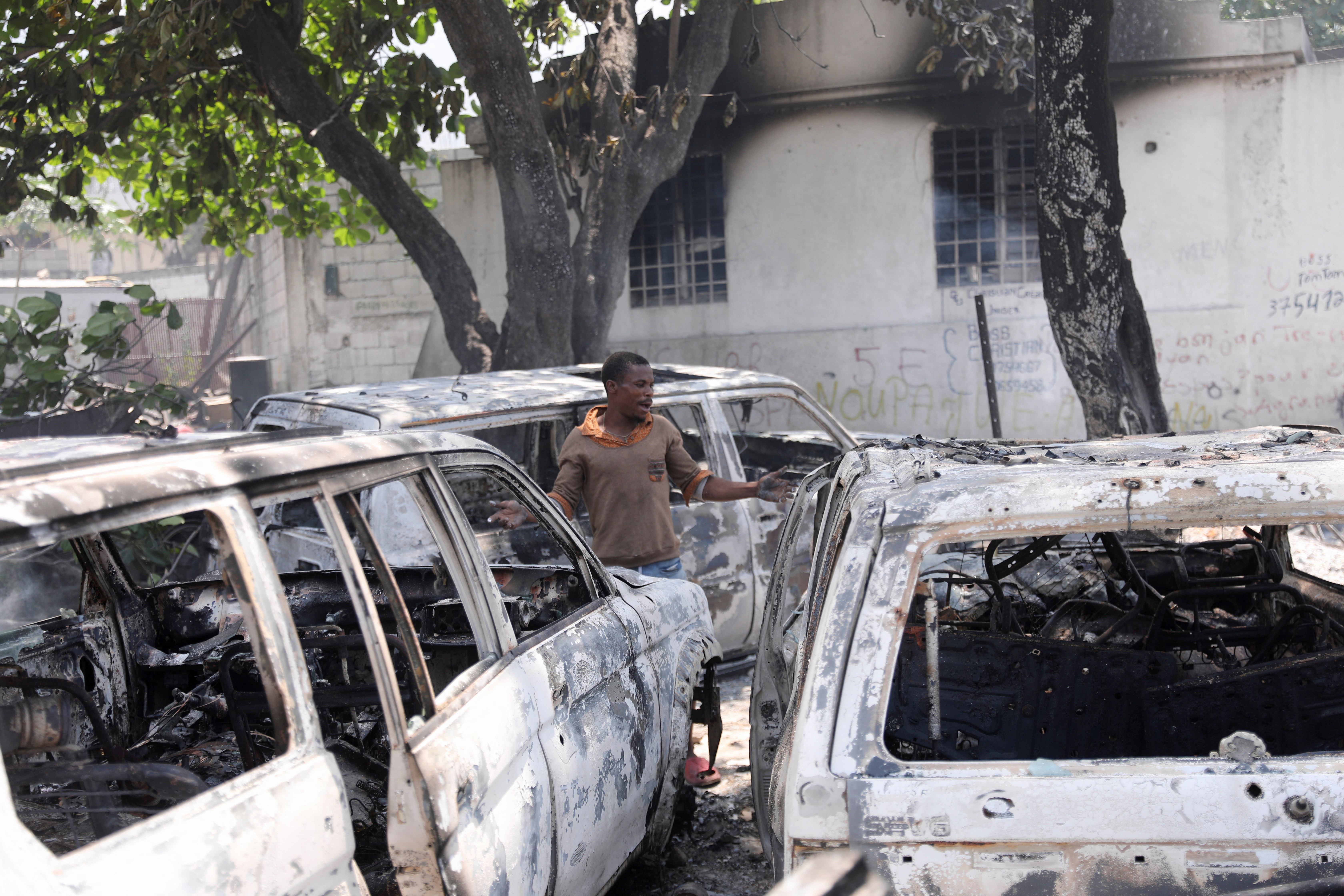 A man reacts next to the charred remains of vehicles near the presidential palace, after they were set on fire by gangs, in Port-au-Prince