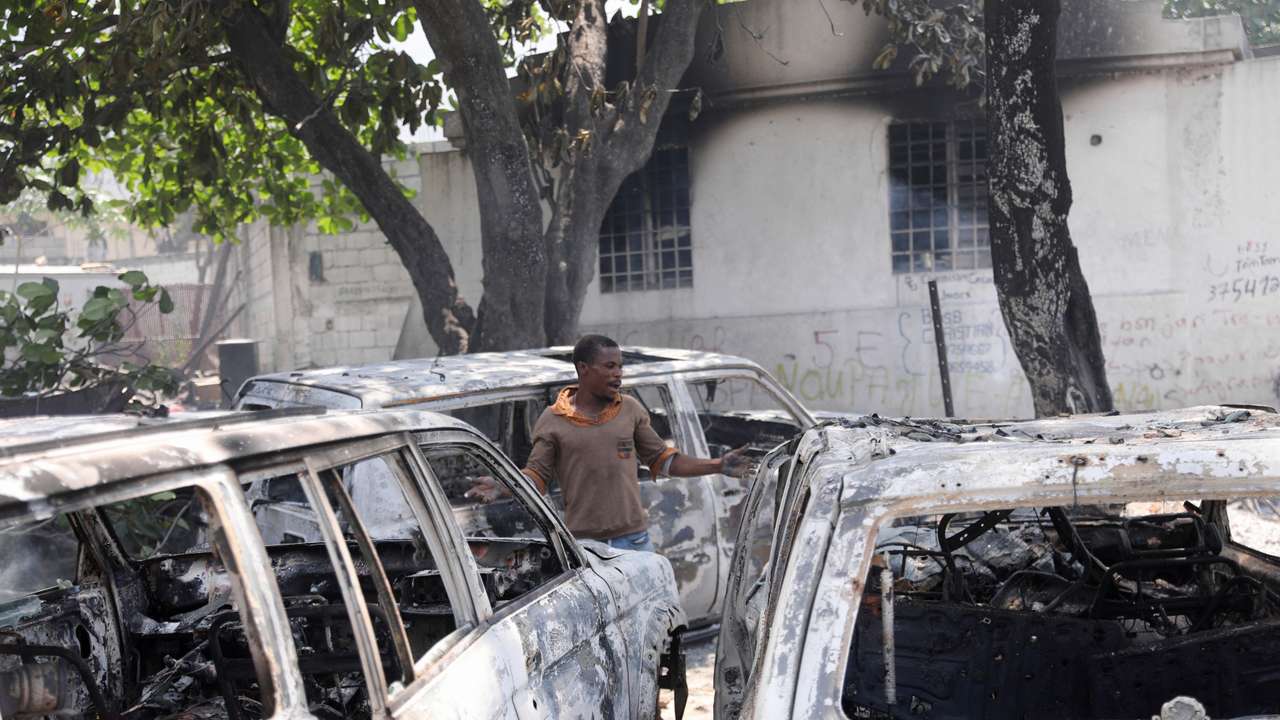 A man reacts next to the charred remains of vehicles near the presidential palace, after they were set on fire by gangs, in Port-au-Prince