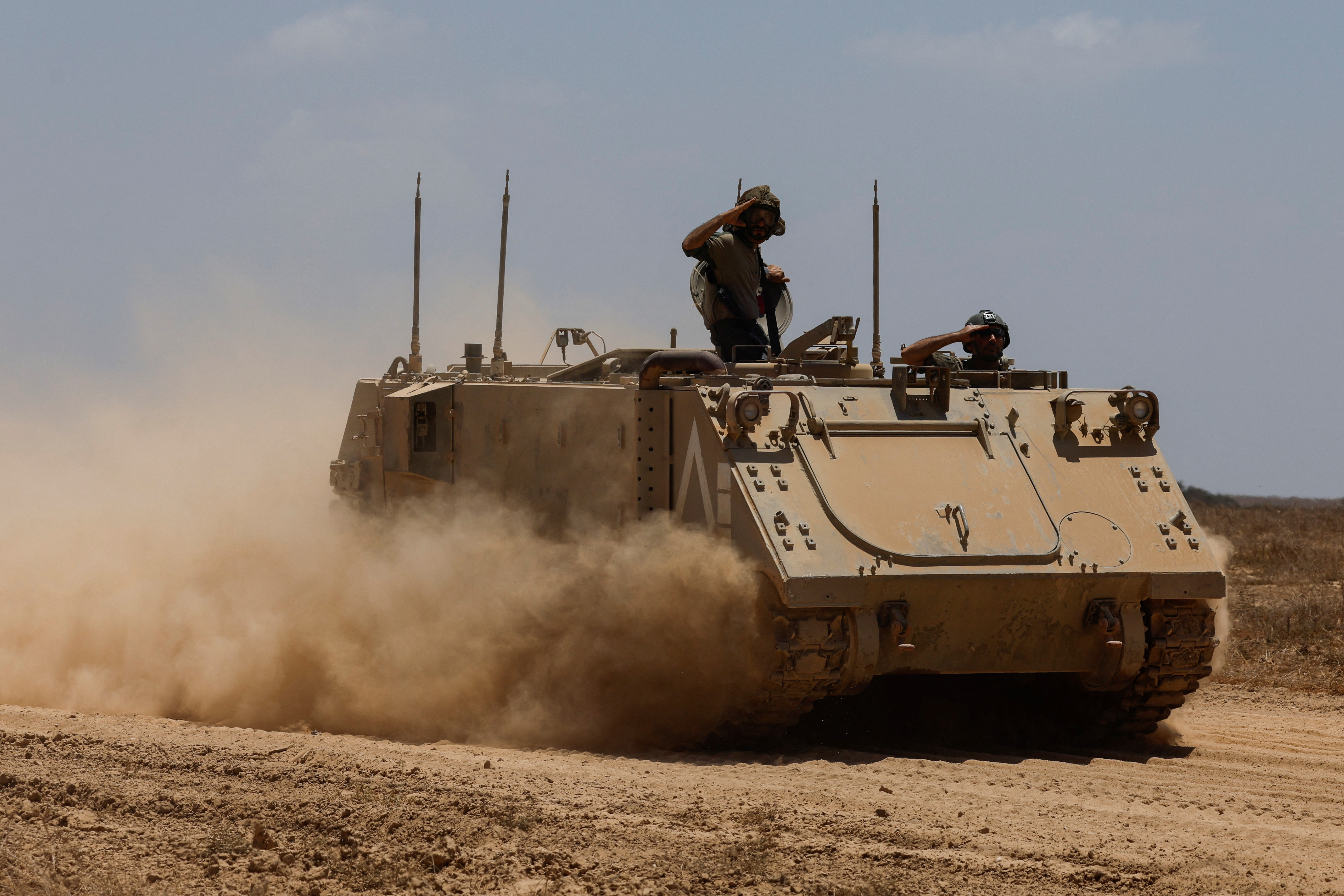 Israeli soldiers salute on a military vehicle as they manoeuvre, near the Israel-Gaza border