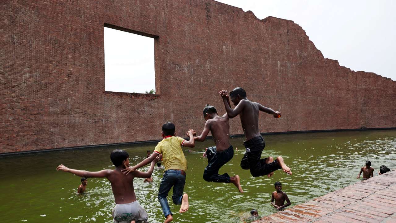 Children jump into the water body of Martyred Intellectuals Memorial at Rayerbazar, to cool themselves during a heatwave in Dhaka