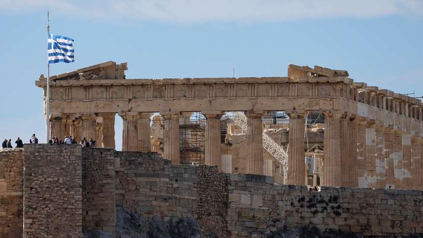 Greek flag flutters in front of the Parthenon Temple atop the Acropolis in Athens