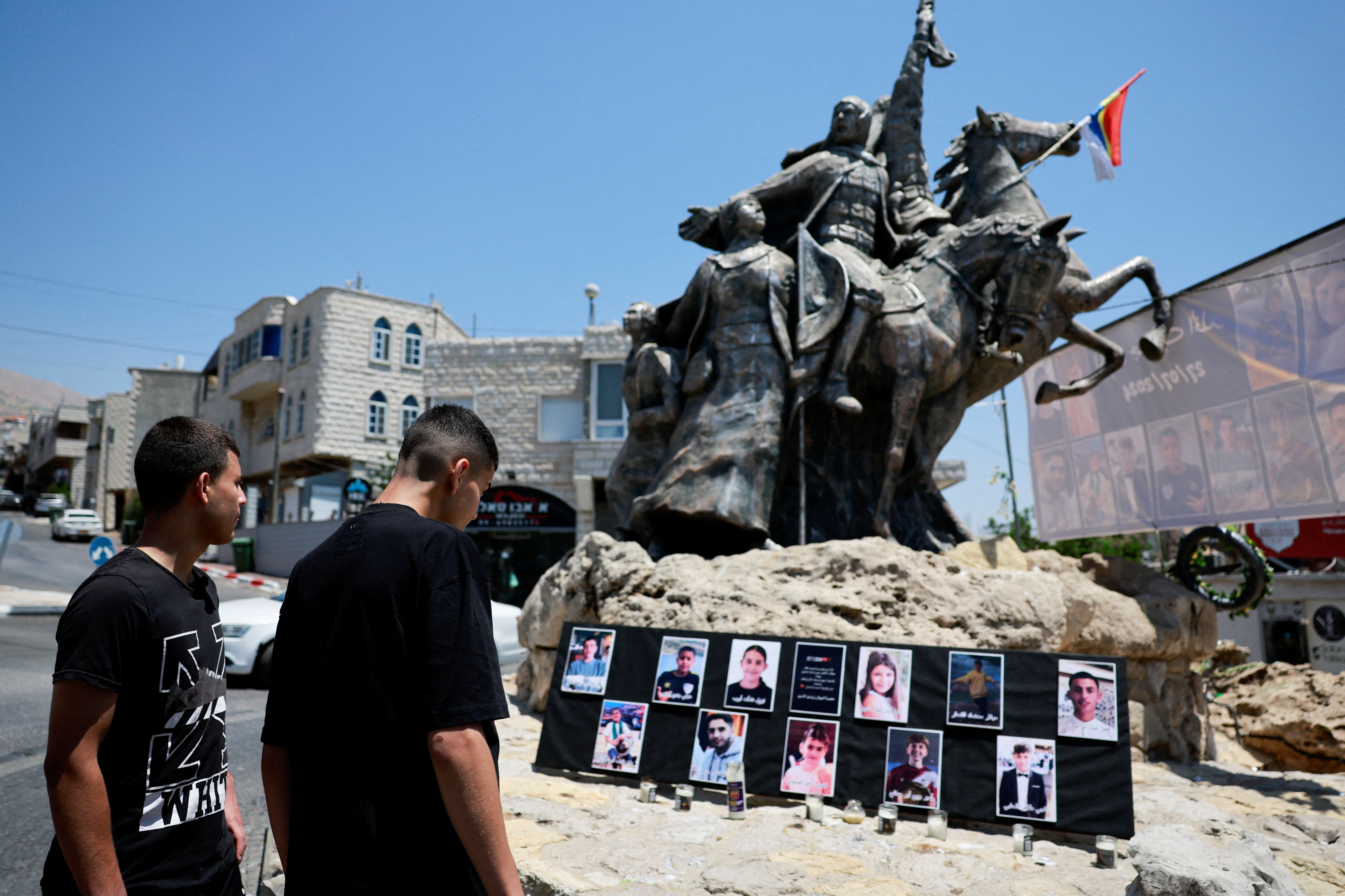 Young people look at the pictures of children and teens killed at a soccer pitch by a rocket Israel says was fired from Lebanon, at a roundabout in Majdal Shams
