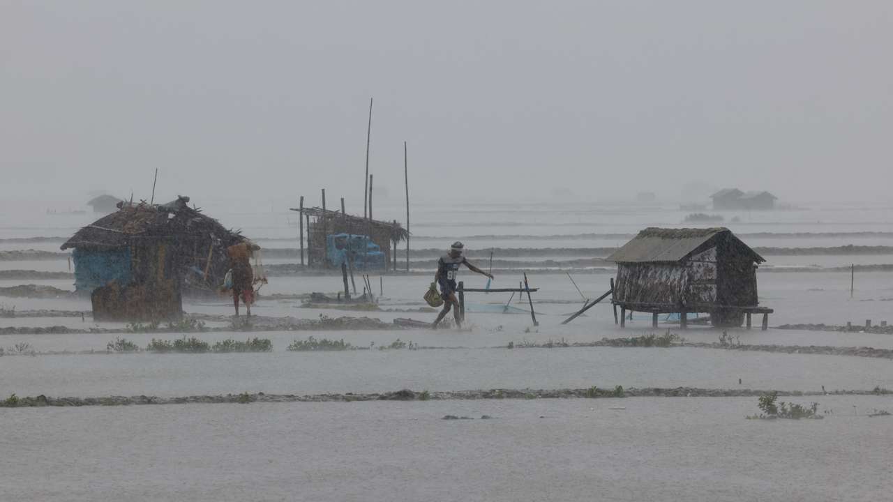 People walk along flooded shrimp and crab farms due to heavy rain as Cyclone Remal passes the country in the Shyamnagar area of Satkhira
