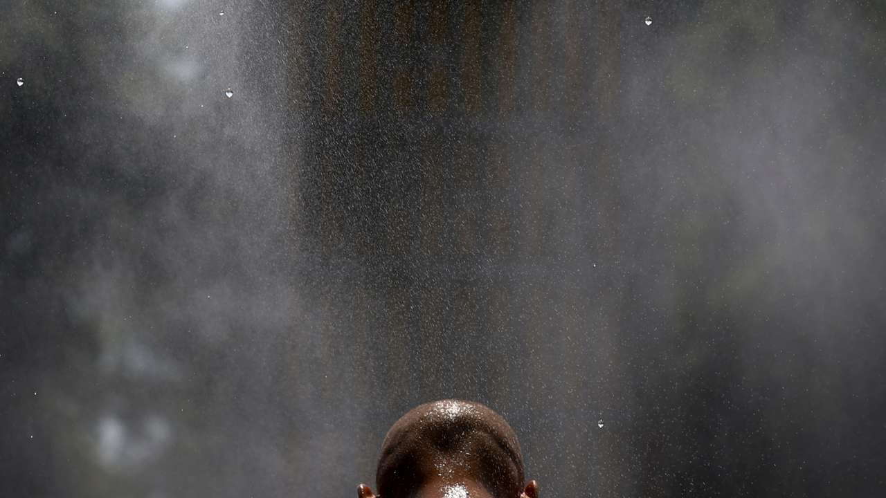 Man cools himself under a water sprinkler on an extremely hot summer day in Kyiv