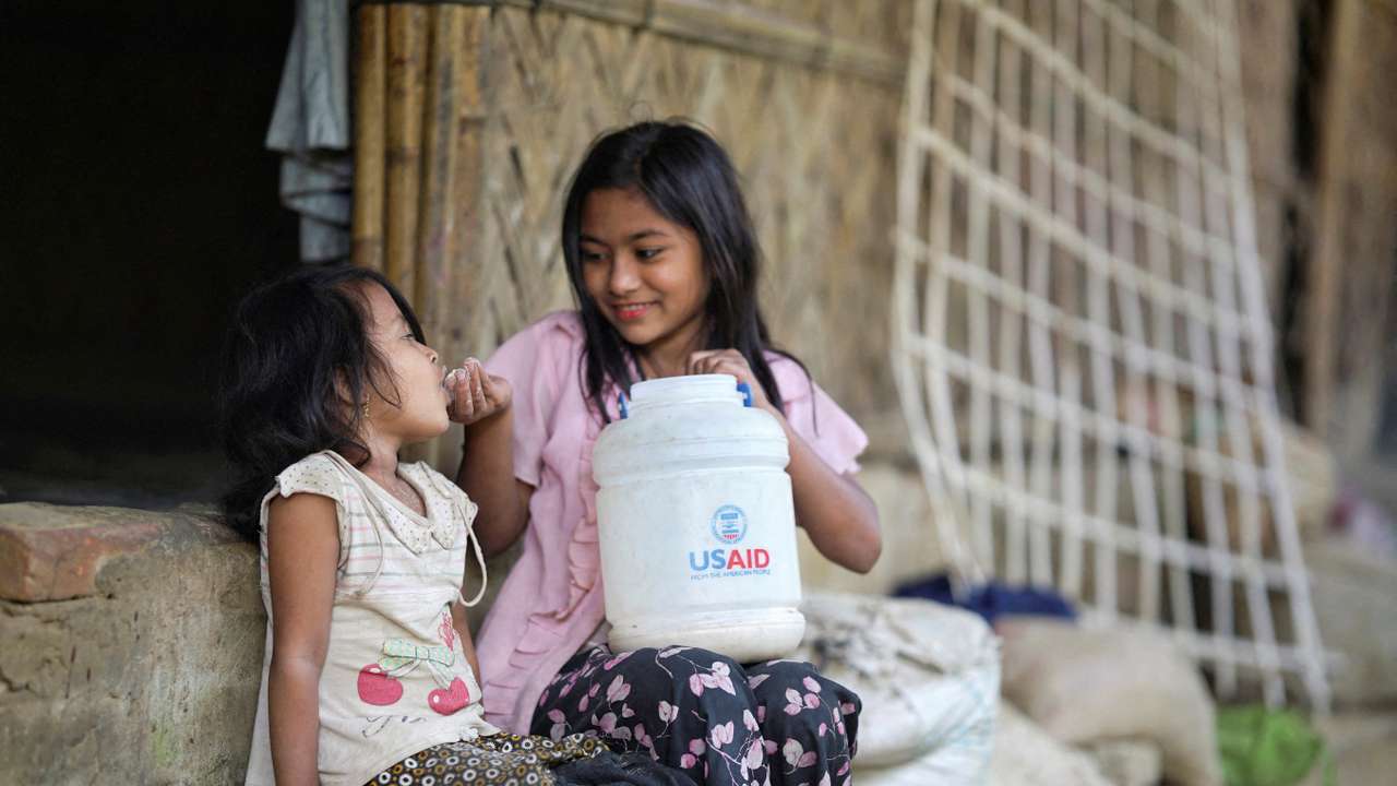 FILE PHOTO: A Rohingya girl feeds a child from a jar with the USAID logo on it at a refugee camp in Cox's Bazar