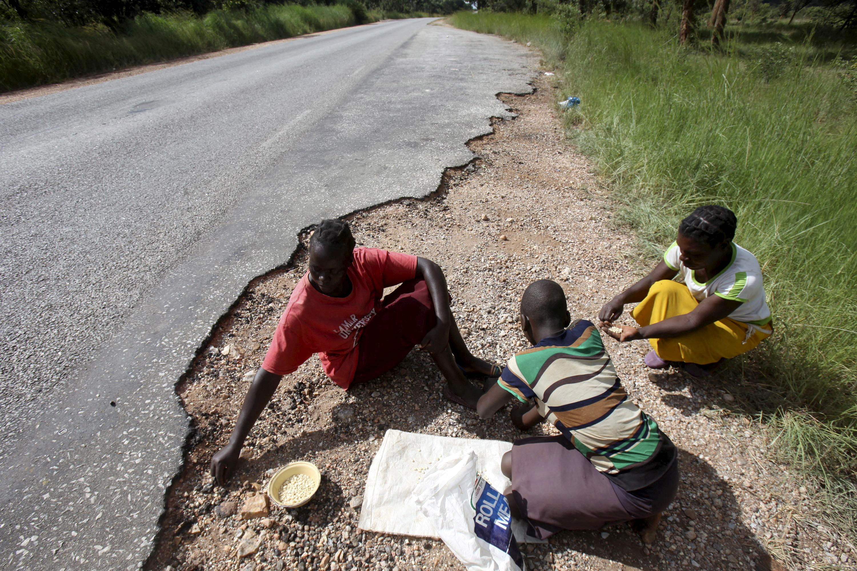 FILE PHOTO: Women gather grain spilled by cargo trucks from Zambia along a highway in Magunje