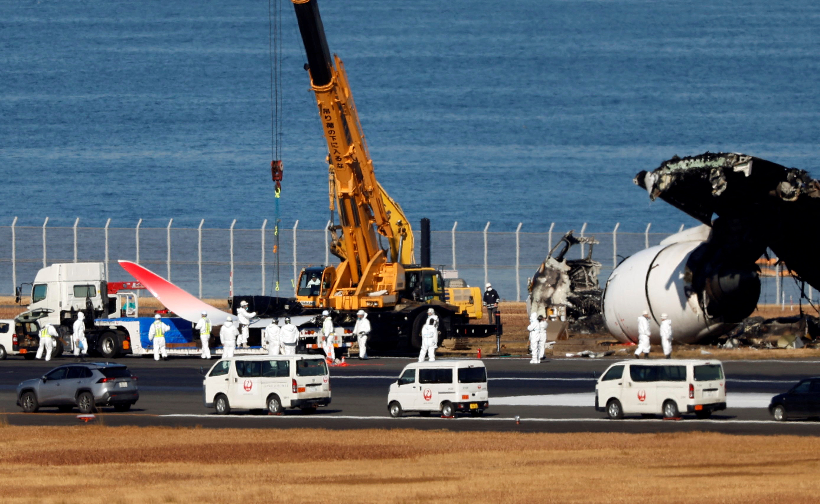 Officials remove the wreckage of a burnt JAL Airbus A350 plane after a collision with a Japan Coast Guard aircraft, in Tokyo