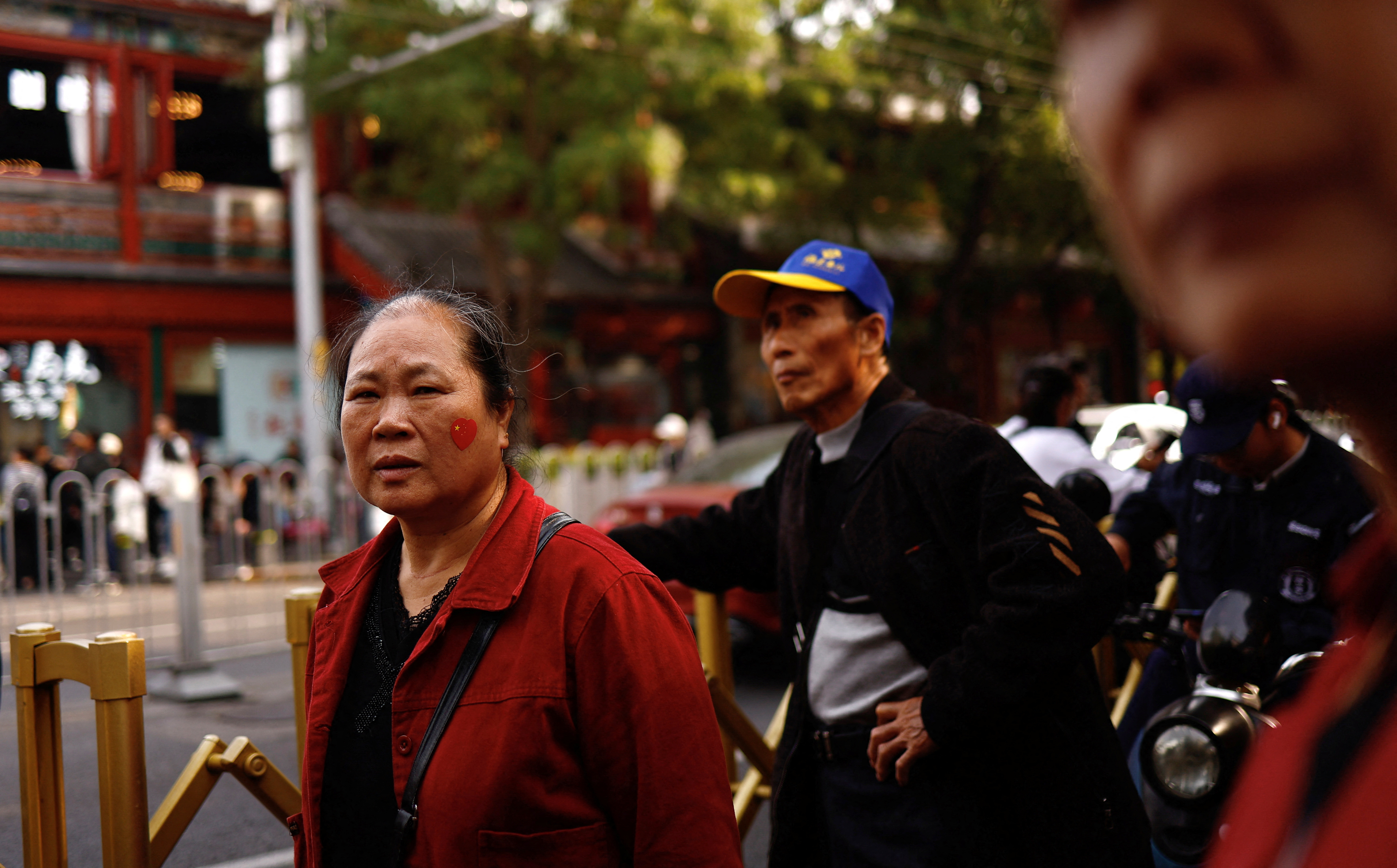 Woman with a sticker of Chinese national flag in a shape of a heart on her face walks on a street in Beijing