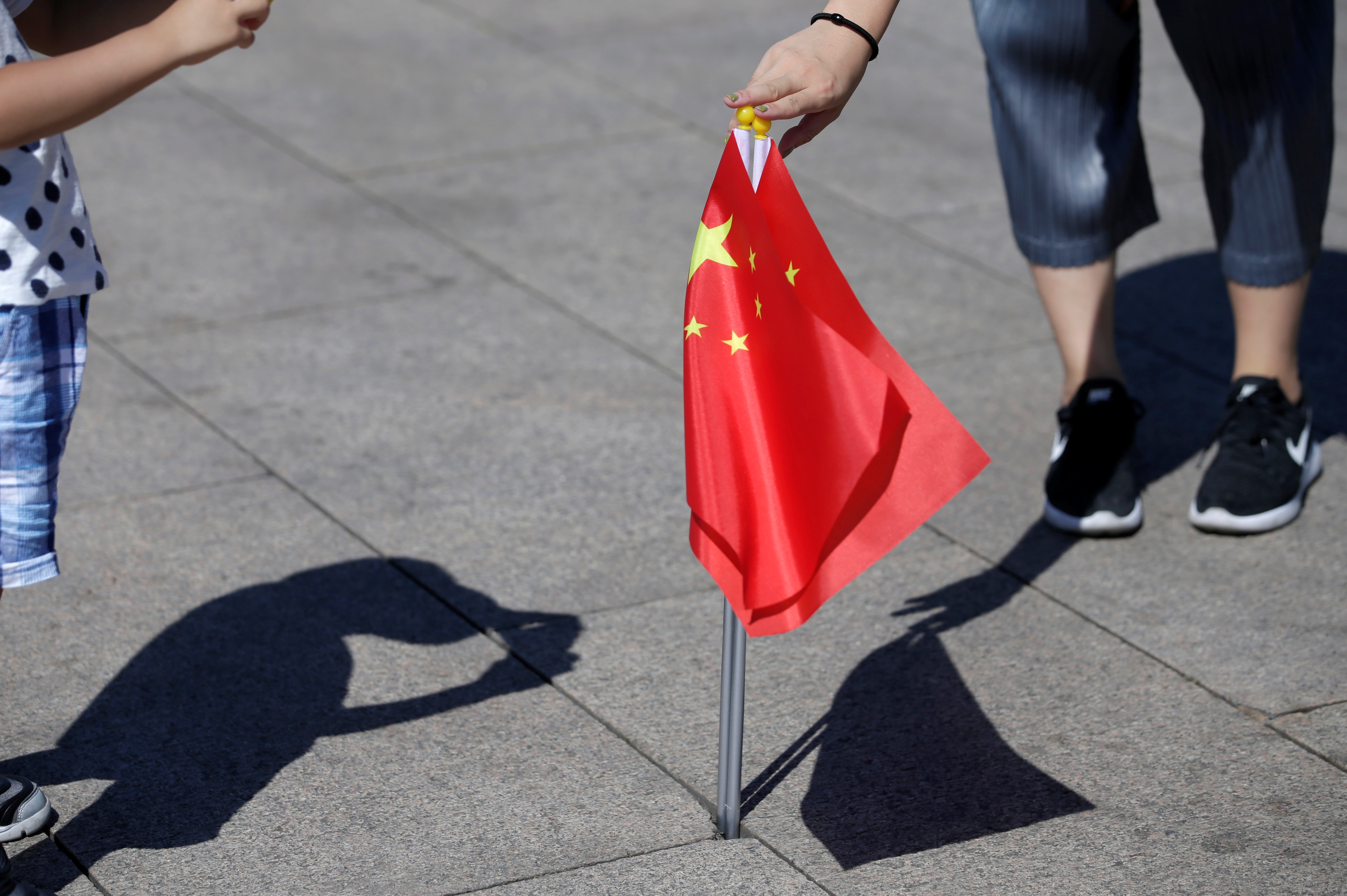 FILE PHOTO: A mother holds Chinese flags as she helps her son take a picture on Tiananmen Square in Beijing
