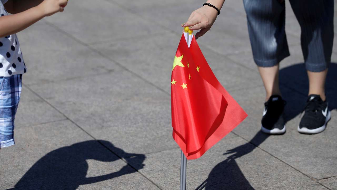 FILE PHOTO: A mother holds Chinese flags as she helps her son take a picture on Tiananmen Square in Beijing