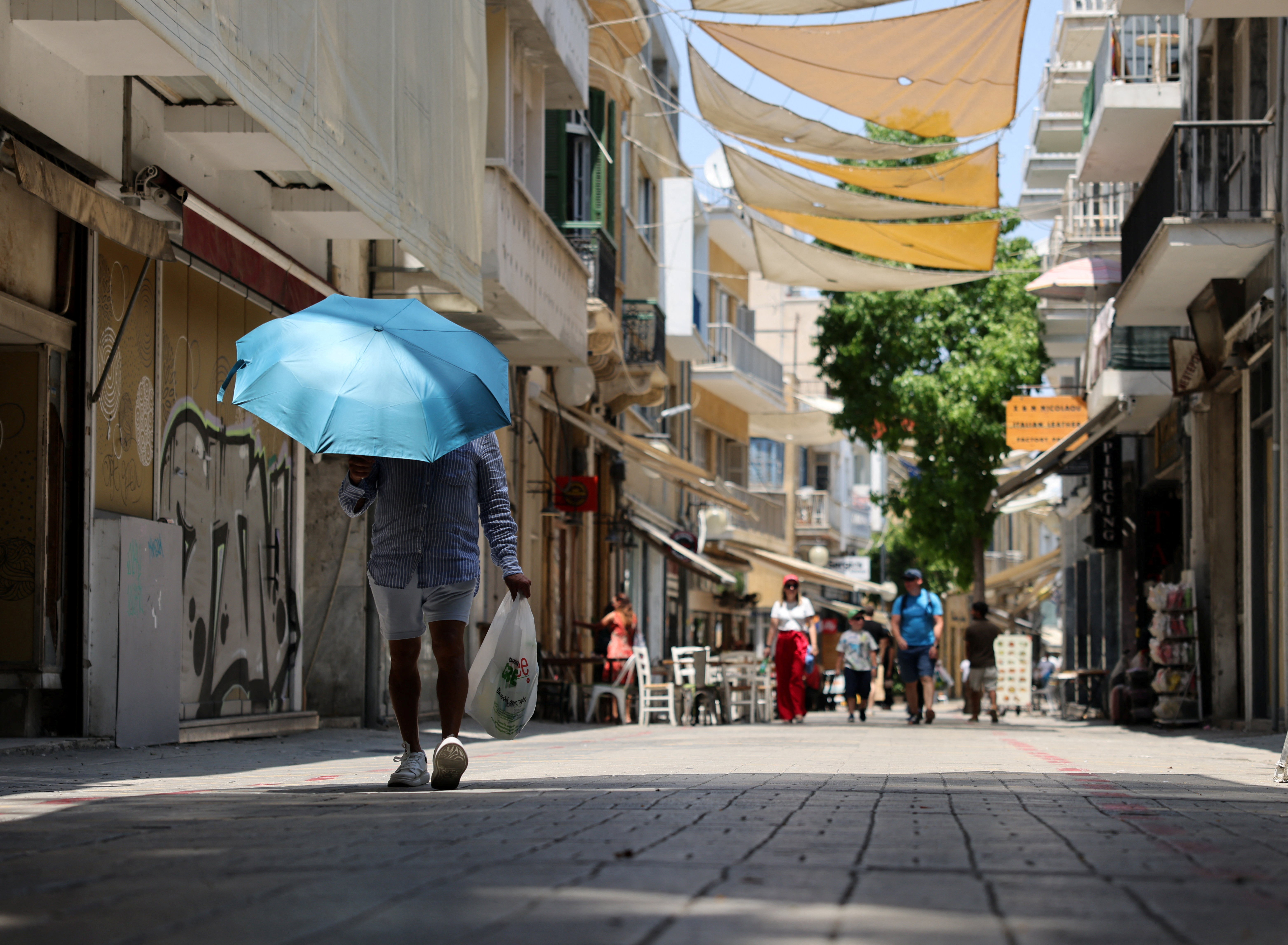 A man shelters from the sun with an umbrella during a heatwave in Nicosia