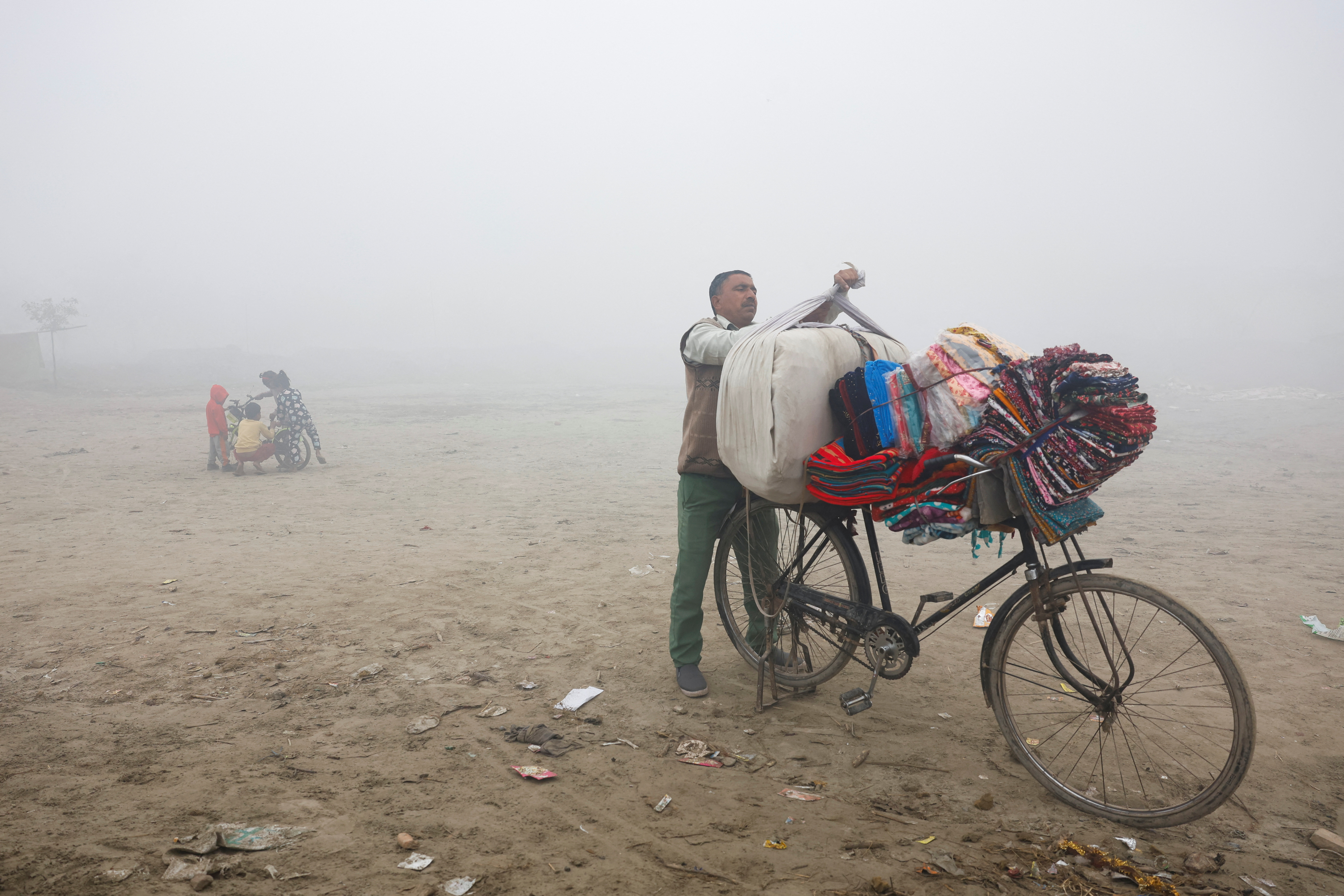 A vendor selling bedsheets loads them onto his bicycle on a foggy and cold winter morning in New Delhi