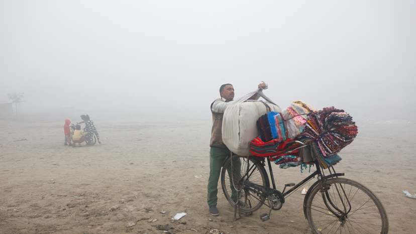 A vendor selling bedsheets loads them onto his bicycle on a foggy and cold winter morning in New Delhi