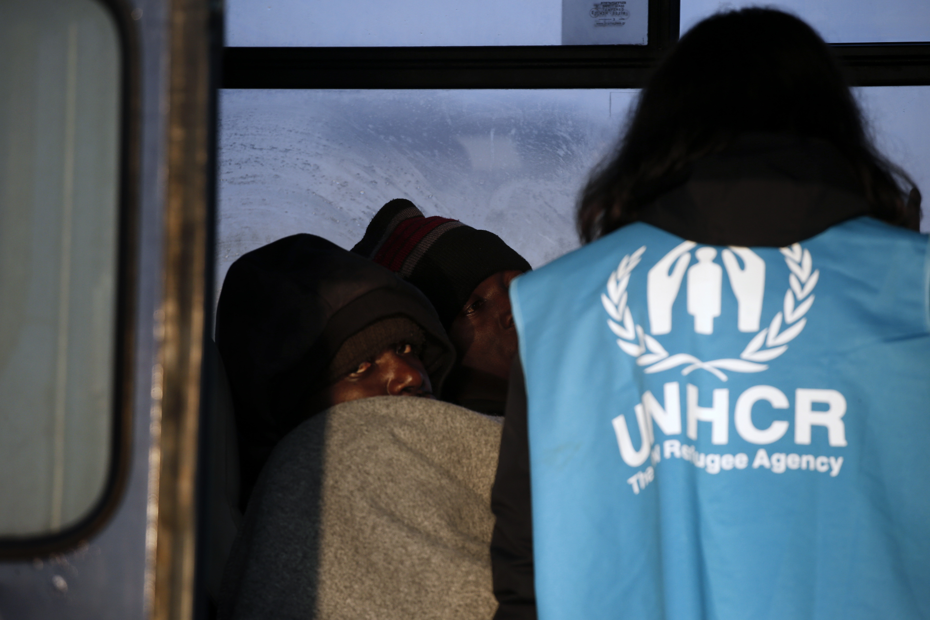 A Congolese refugee looks on as a UNHCR volunteer checks on refugees and migrants rescued at open sea and waiting to be transferred to the Moria registration centre at the port of Mytilene on the Lesbos island