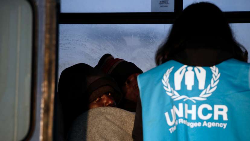 A Congolese refugee looks on as a UNHCR volunteer checks on refugees and migrants rescued at open sea and waiting to be transferred to the Moria registration centre at the port of Mytilene on the Lesbos island
