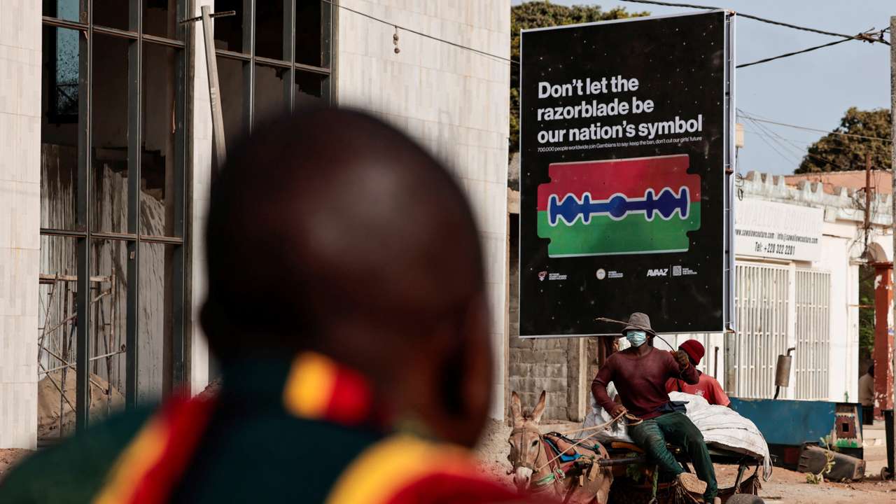 People ride past a poster advocating for the end of female genital mutilation (FGM), in Banjul