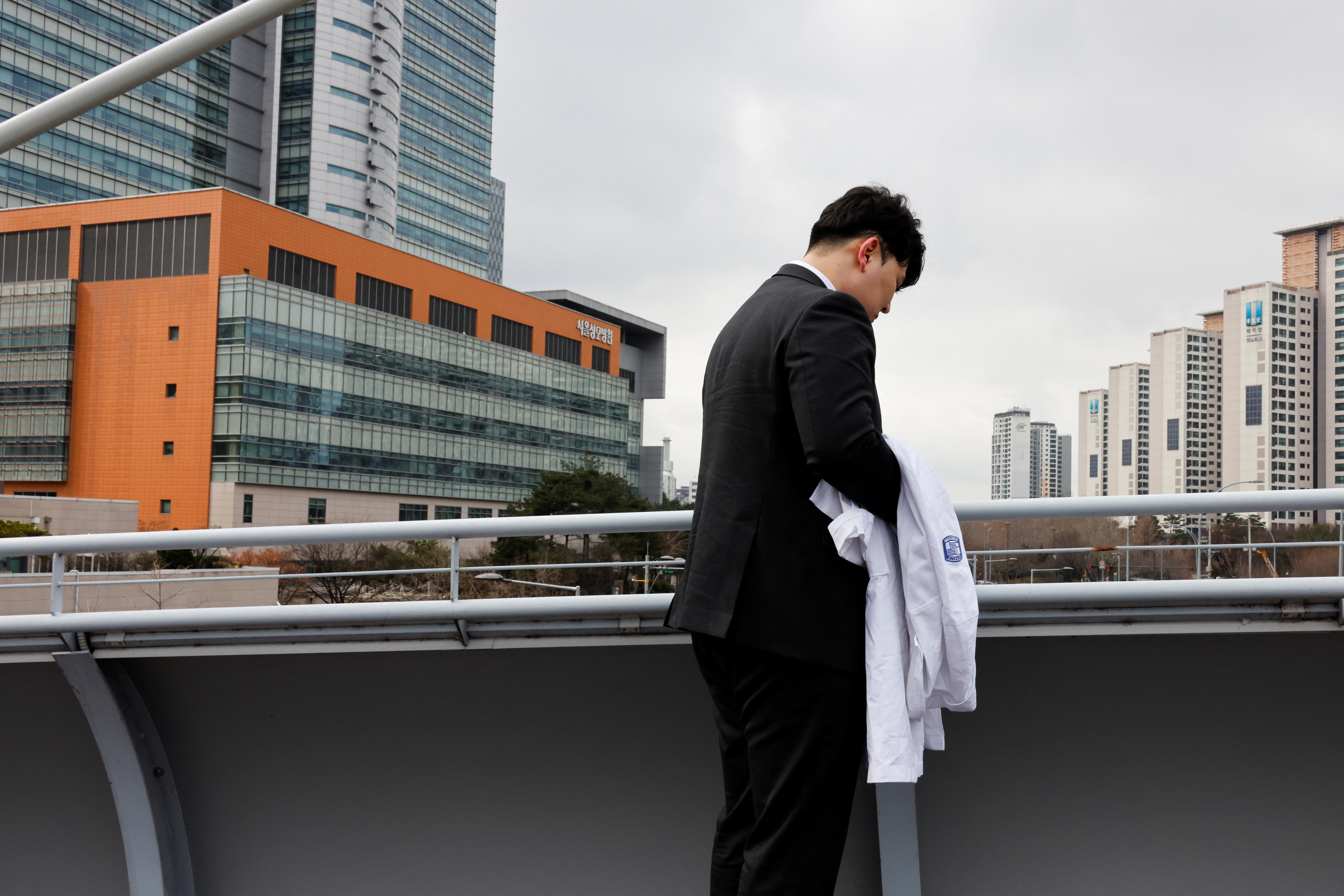 One of thousands of South Korean trainee doctors who resigned en masse to protest the government's medical policy, holds his white coat in front of the hospital where he worked in Seoul