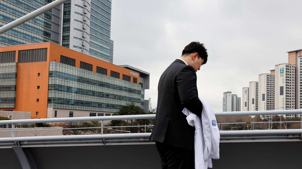 One of thousands of South Korean trainee doctors who resigned en masse to protest the government's medical policy, holds his white coat in front of the hospital where he worked in Seoul