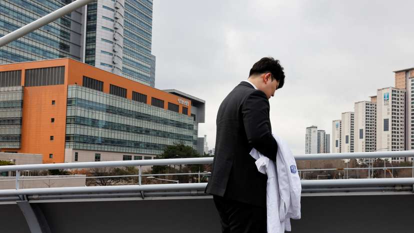 One of thousands of South Korean trainee doctors who resigned en masse to protest the government's medical policy, holds his white coat in front of the hospital where he worked in Seoul