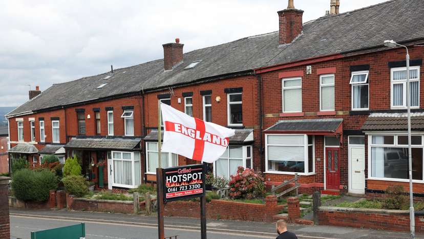 A man walks past a flag bearing the colours of England's St. George's Cross, flying above a residential street in Radcliffe, near Manchester,