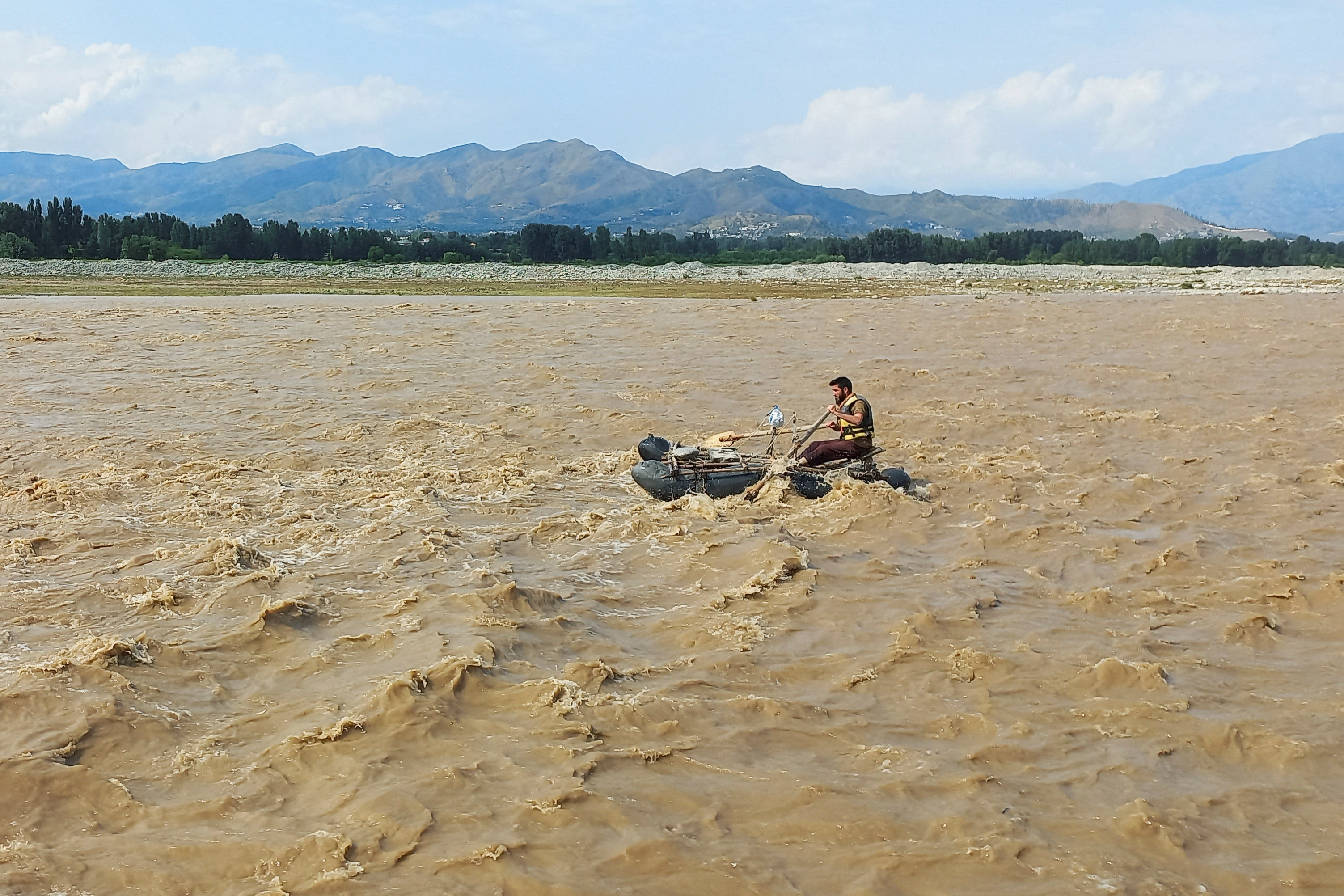 A rescue worker rows a raft while searching for survivors, after tourists, who were on a picnic, were swept away by overflowing floodwaters in the Swat River