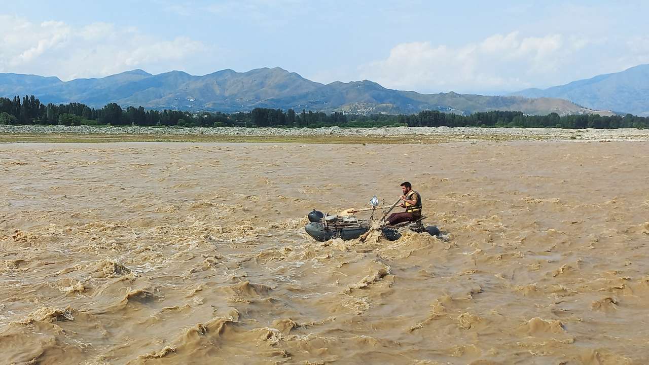 A rescue worker rows a raft while searching for survivors, after tourists, who were on a picnic, were swept away by overflowing floodwaters in the Swat River