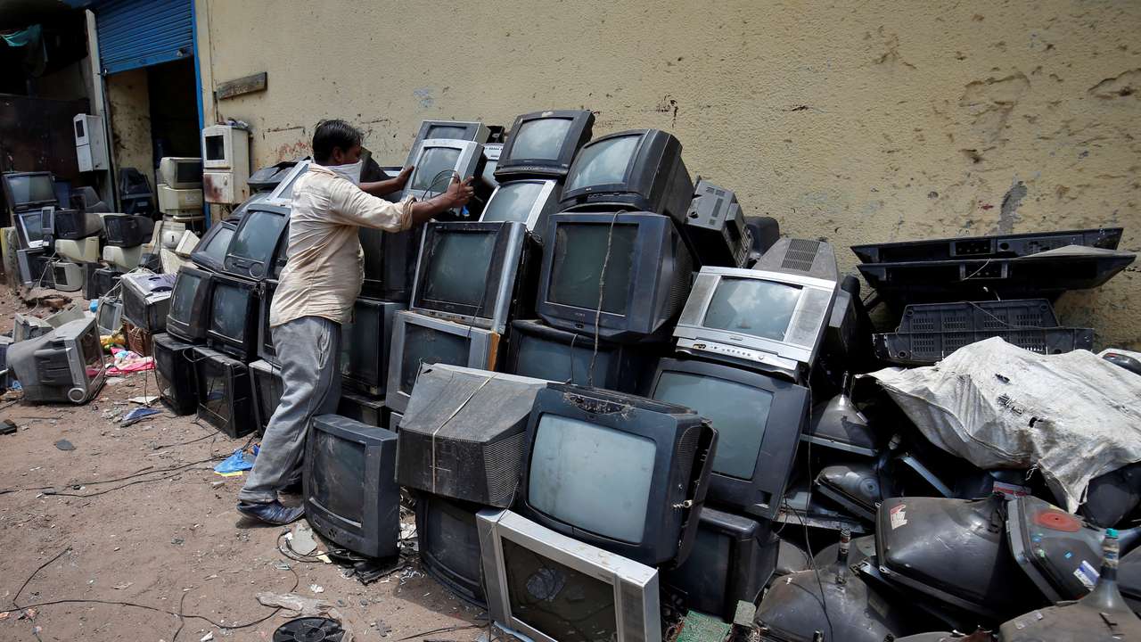A scrap dealer piles up discarded TV sets before dismantling them at a scrap yard in Ahmedabad