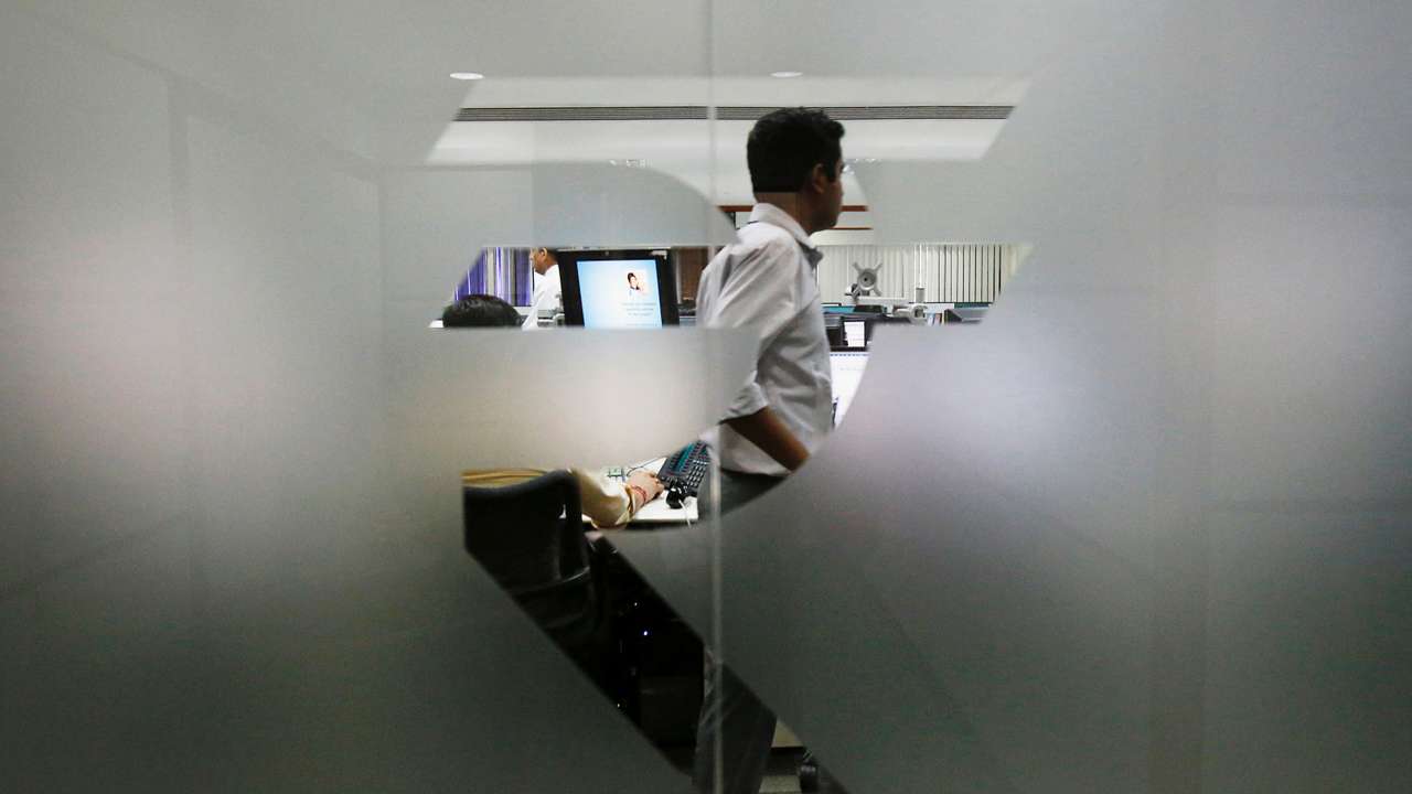 FILE PHOTO: A currency trader is pictured through the symbol for the Indian Rupee on the floor of a trading firm in Mumbai
