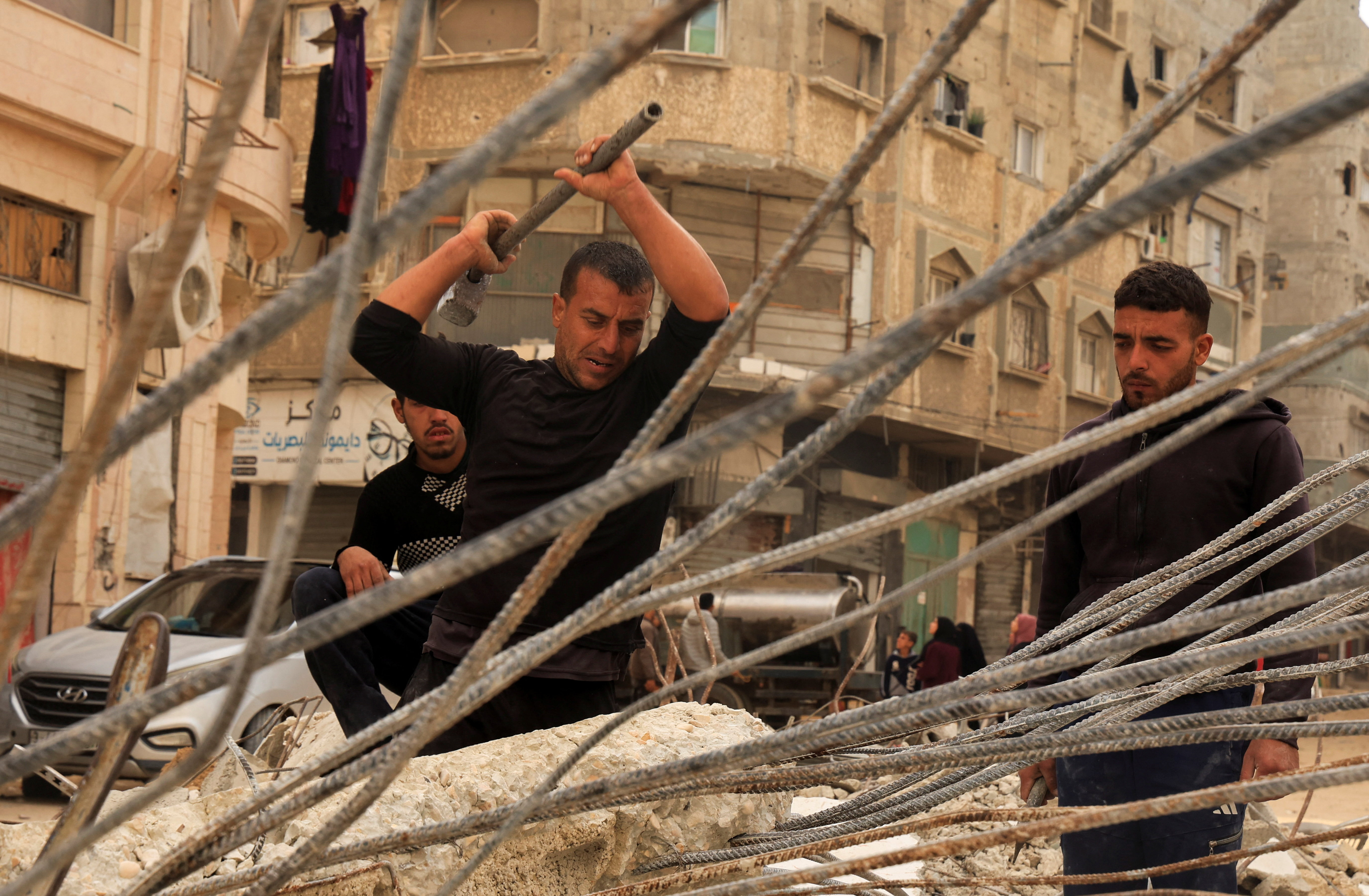 Palestinian workers break concrete to extract steel bars from destroyed homes, relying only on simple hand tools amid a severe shortage of construction materials caused by long-standing restrictions on the entry of cement and iron, in Khan Younis