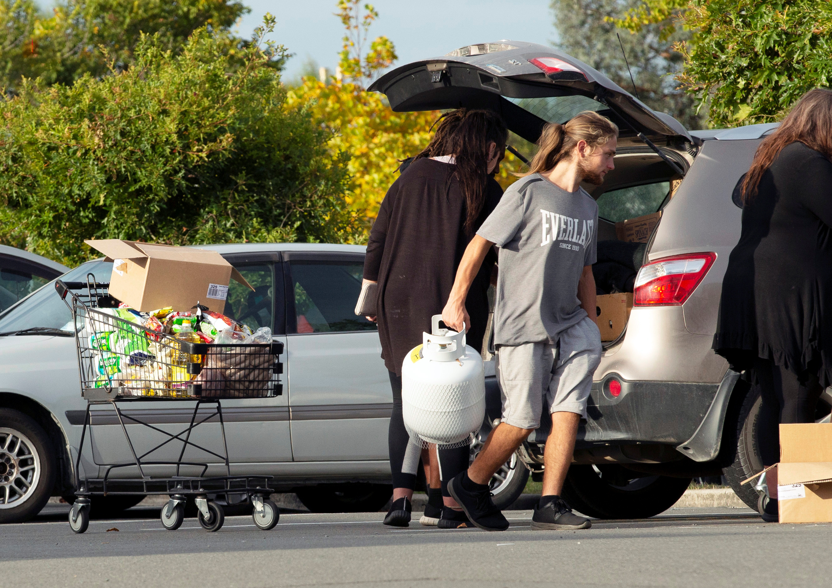 People take out products from their supermarket shopping cart and load them into their car outside Pak'nSave supermarket
