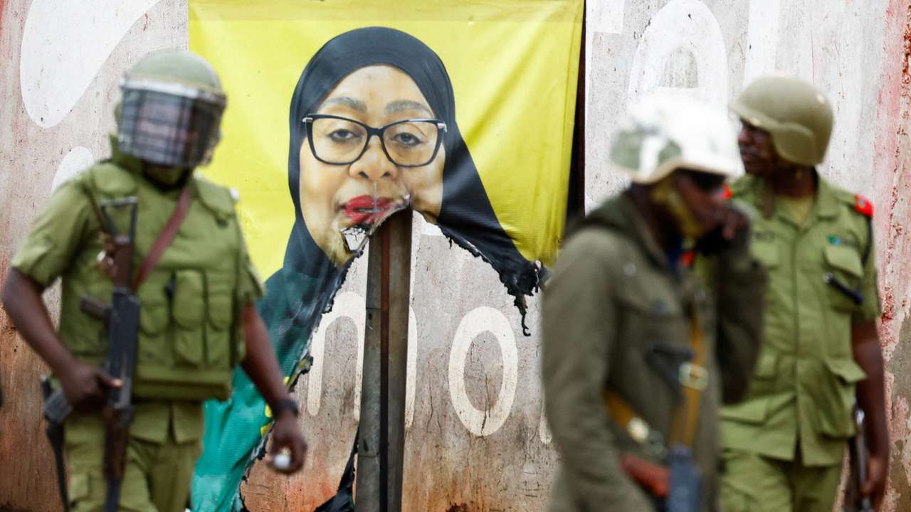 Tanzanian riot police officers walk past a vandalised campaign poster of President Samia Suluhu Hassan, following a protest a day after a general election marred by violent demonstrations over the exclusion of two leading opposition candidates at the Namanga One-Post Border crossing point between Kenya and Tanzania, October 30, 2025. REUTERS/Thomas Mukoya