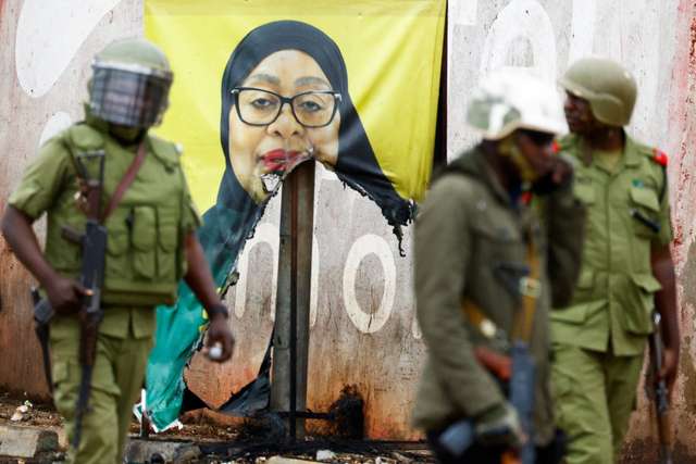 Tanzanian riot police officers walk past a vandalised campaign poster of President Samia Suluhu Hassan, following a protest a day after a general election marred by violent demonstrations over the exclusion of two leading opposition candidates at the Namanga One-Post Border crossing point between Kenya and Tanzania, October 30, 2025. REUTERS/Thomas Mukoya