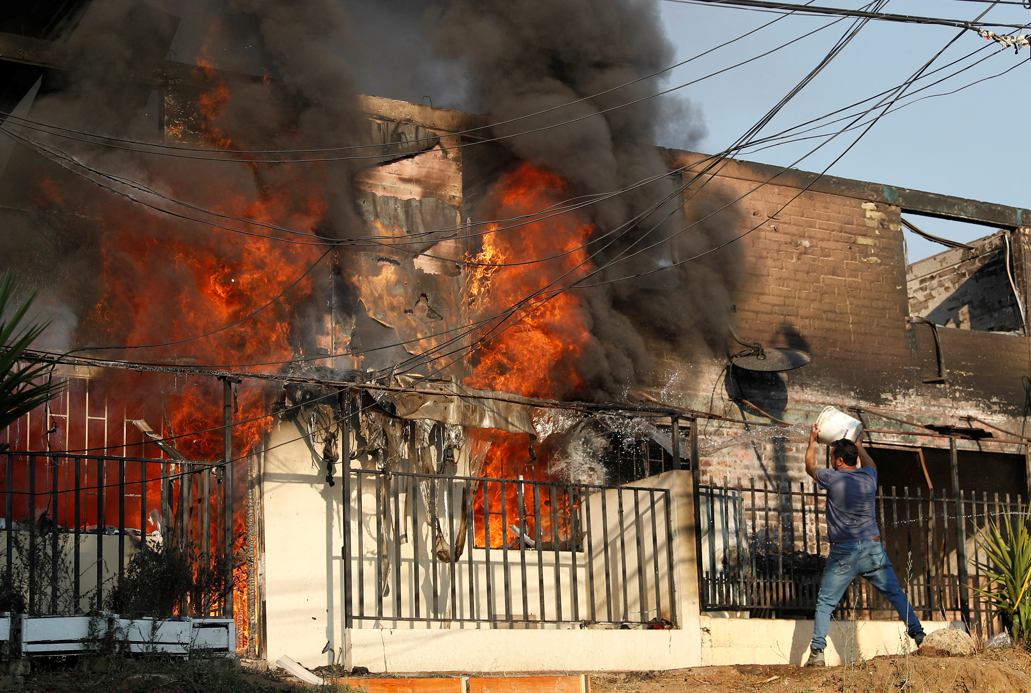 A man tries to extinguish a fire burning a house during the spread of wildfires in Vina del Mar