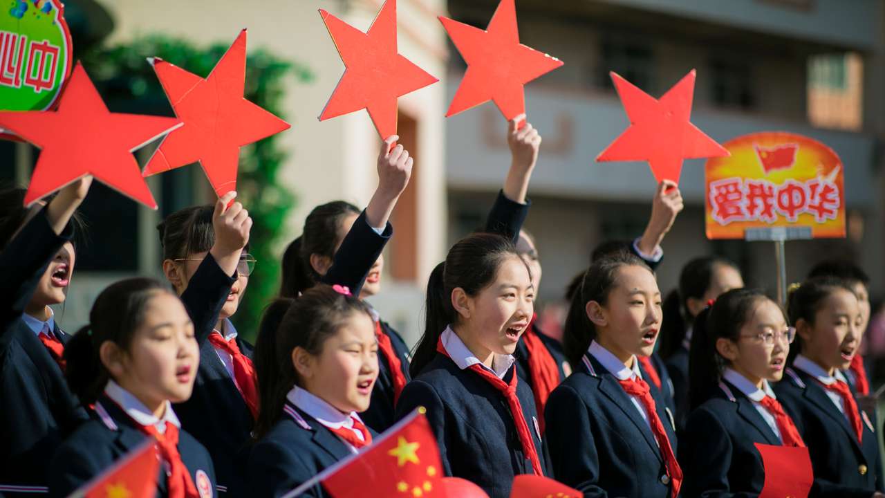 Students hold Chinese flags and cutouts of red stars as they perform a song titled "Me and my country", at a ceremony marking the primary school's new semester in Hohhot