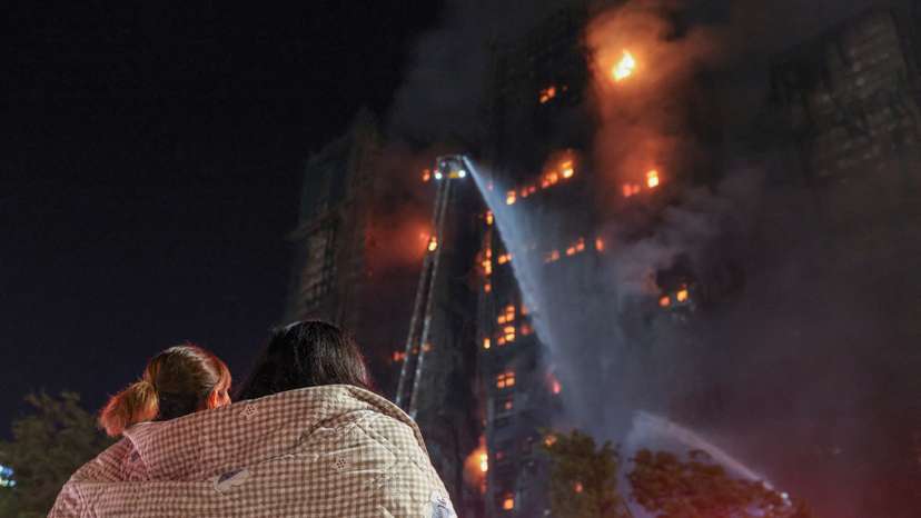Residents wrapped in blankets watch flames engulf bamboo scaffolding at Wang Fuk Court housing estate after a major fire broke out, in Tai Po, Hong Kong