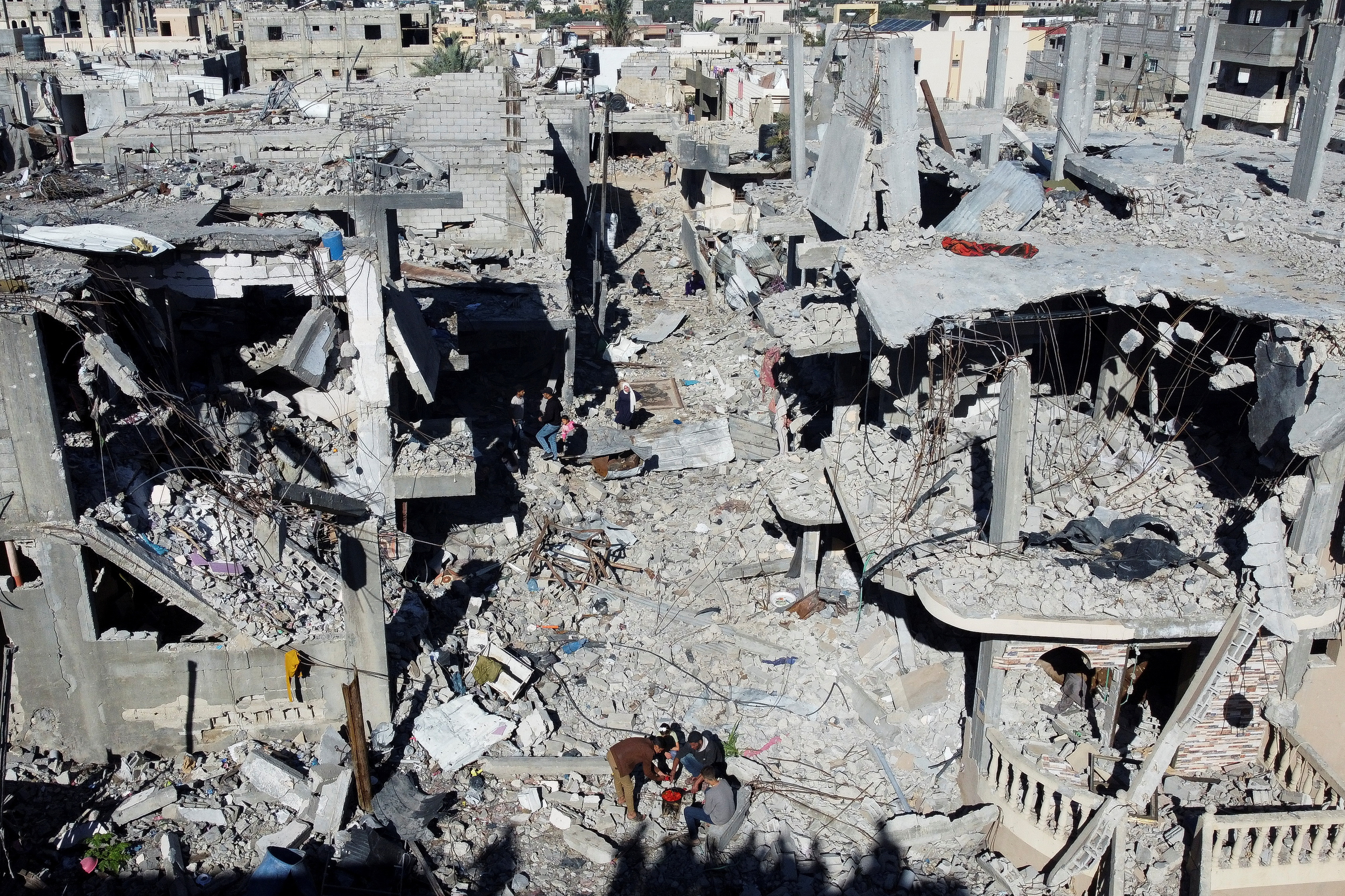 Palestinians cook among the houses destroyed in Israeli strikes, at Khan Younis refugee camp