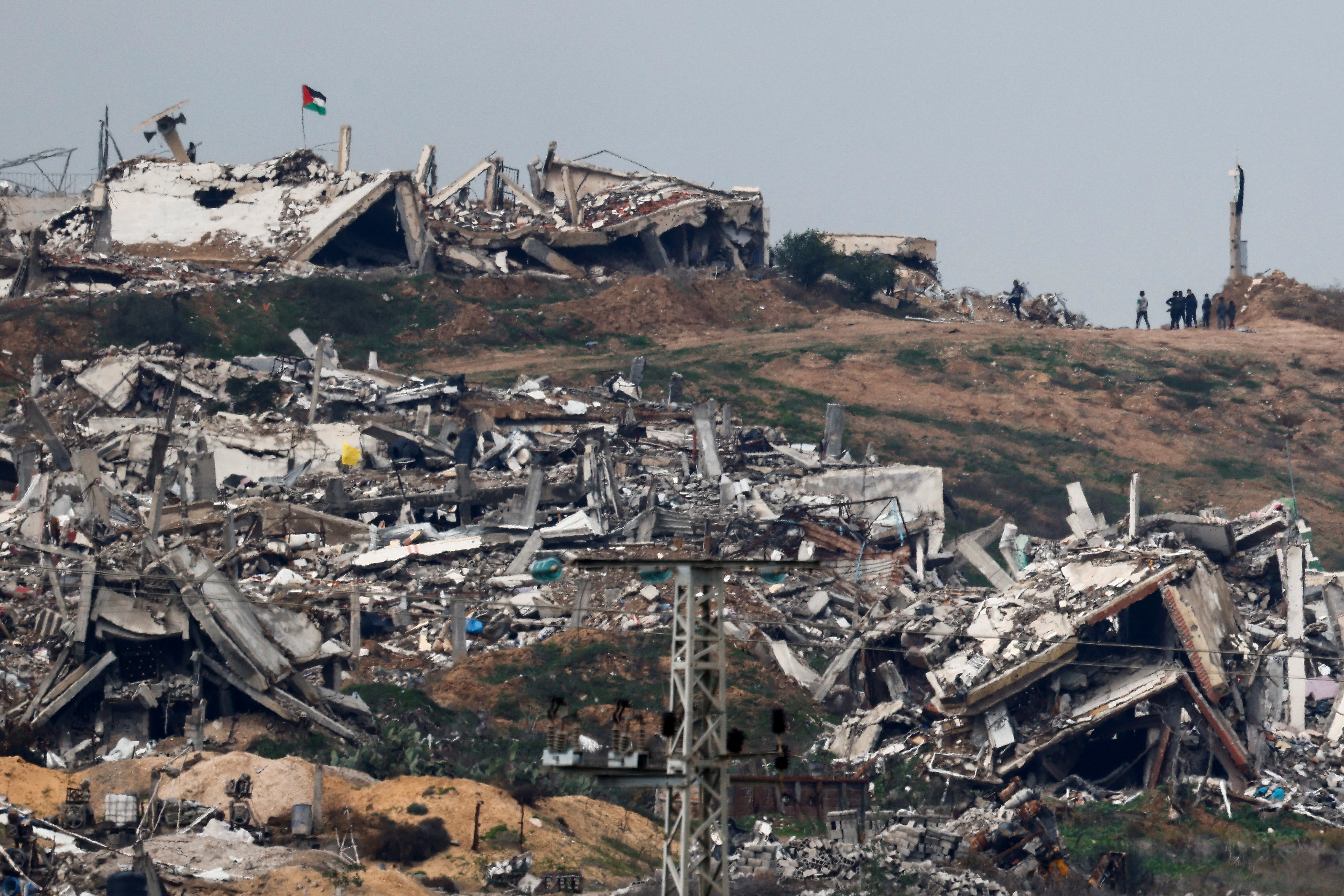 Palestinian flag flutters as people walk near buildings in ruins in Gaza, as seen from Israel